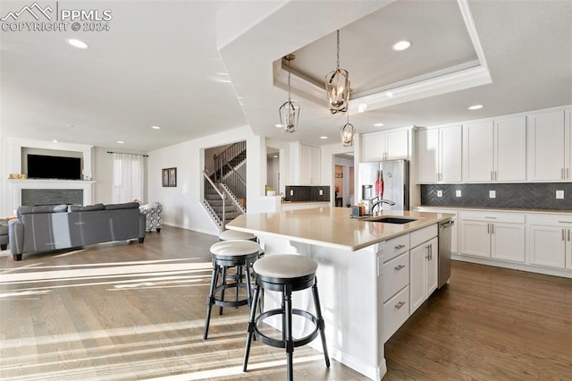 kitchen with backsplash, stainless steel appliances, white cabinets, hanging light fixtures, and an island with sink