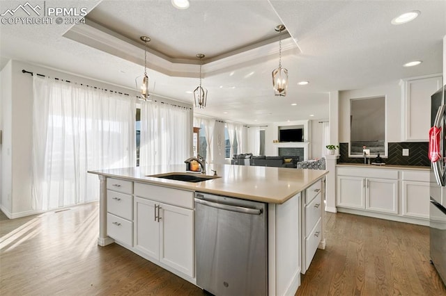 kitchen featuring appliances with stainless steel finishes, sink, decorative light fixtures, white cabinetry, and an island with sink