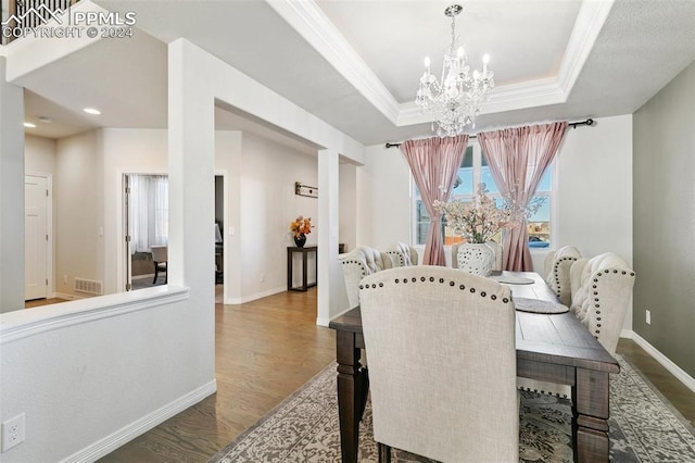 dining room featuring wood-type flooring, a raised ceiling, ornamental molding, and a notable chandelier