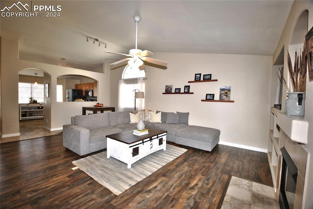 living room with rail lighting, ceiling fan, dark wood-type flooring, and vaulted ceiling