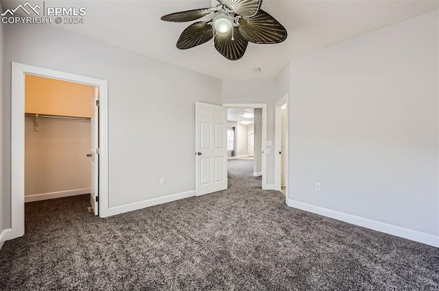 unfurnished bedroom featuring dark colored carpet, ceiling fan, a walk in closet, and a closet