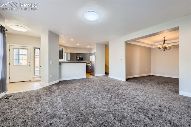 unfurnished living room featuring a raised ceiling, light colored carpet, and an inviting chandelier