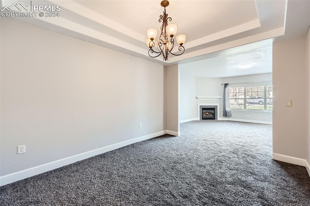 unfurnished living room with a chandelier, dark carpet, and a raised ceiling