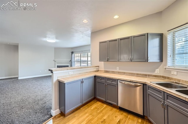 kitchen with kitchen peninsula, light wood-type flooring, stainless steel dishwasher, and gray cabinetry