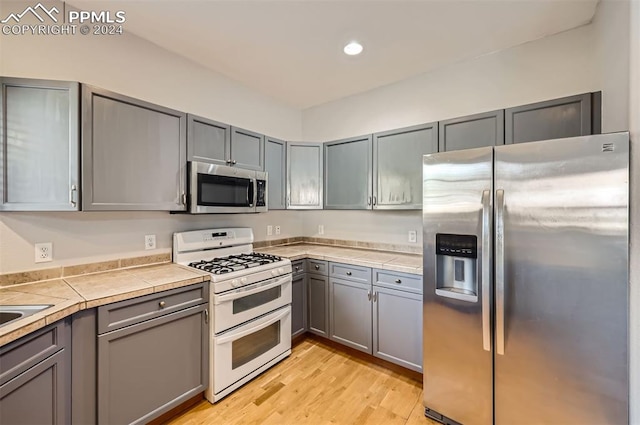 kitchen with gray cabinetry, tile counters, light hardwood / wood-style flooring, and stainless steel appliances