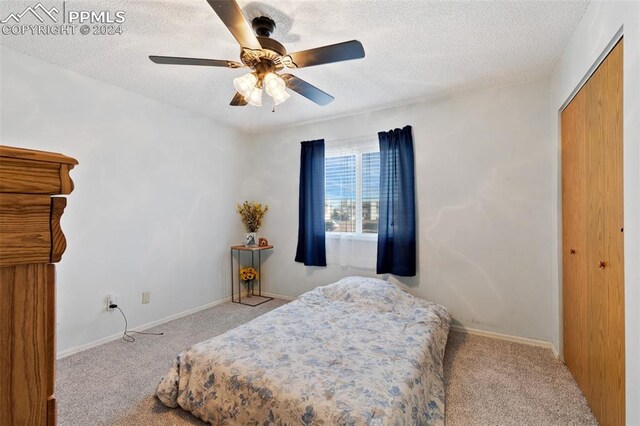 bedroom with ceiling fan, a closet, light colored carpet, and a textured ceiling