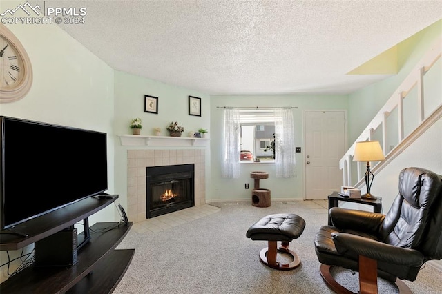 living room with a tiled fireplace, light carpet, and a textured ceiling