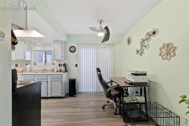 home office featuring a textured ceiling, light hardwood / wood-style floors, ceiling fan, and sink