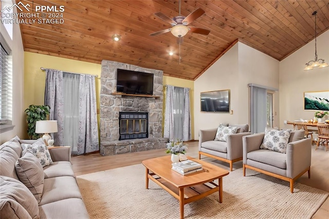 living room featuring ceiling fan with notable chandelier, light hardwood / wood-style floors, a stone fireplace, and wood ceiling