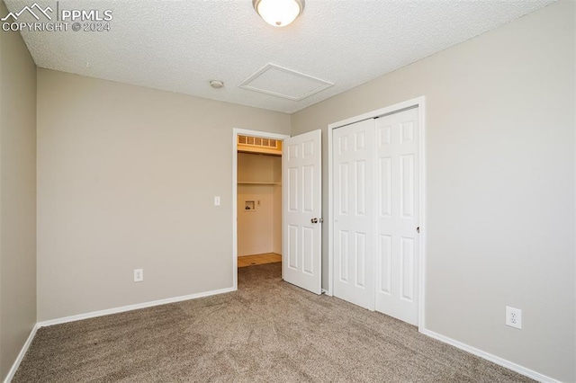 unfurnished bedroom featuring a textured ceiling, a closet, carpet, baseboards, and attic access