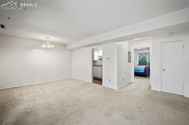 carpeted empty room featuring a textured ceiling and a chandelier