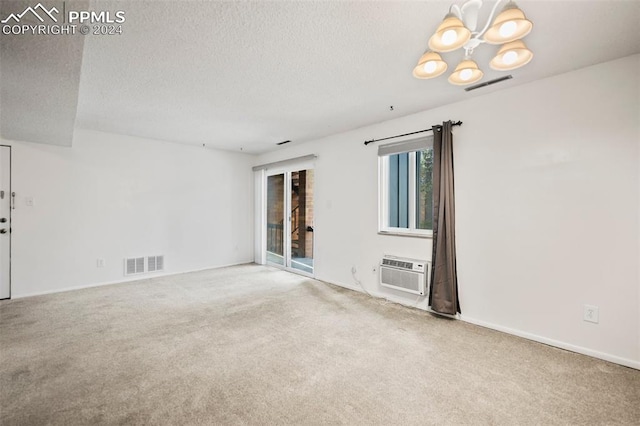 spare room with a wall unit AC, an inviting chandelier, carpet, and a textured ceiling