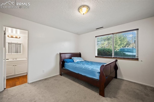 bedroom featuring carpet, ensuite bathroom, and a textured ceiling