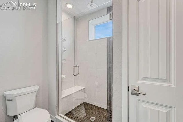 bathroom featuring a shower with door and toilet