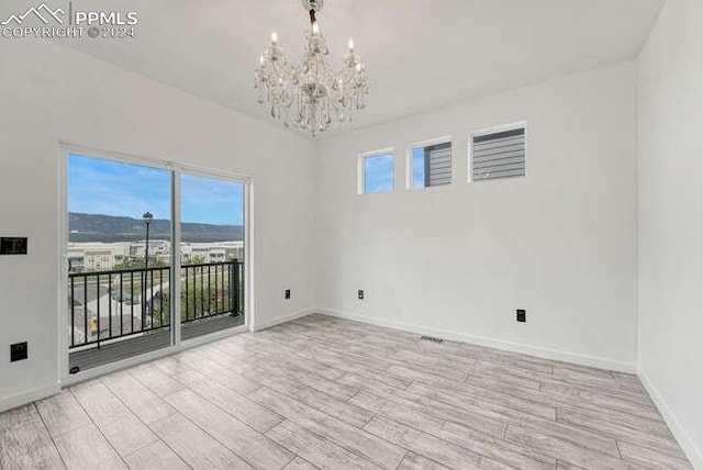 spare room with a mountain view, an inviting chandelier, and light wood-type flooring