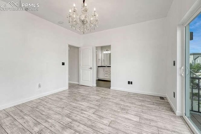 unfurnished room featuring a notable chandelier and light wood-type flooring