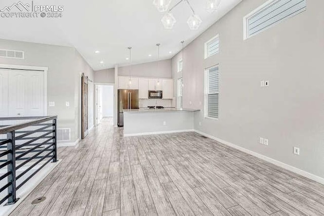 unfurnished living room with a towering ceiling, a notable chandelier, and light wood-type flooring