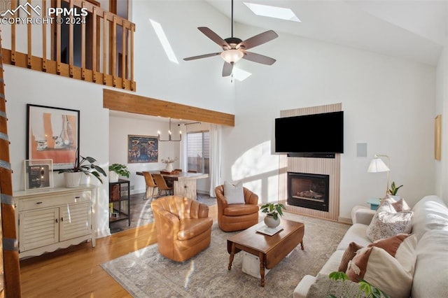 living room featuring high vaulted ceiling, a skylight, ceiling fan, light wood-type flooring, and a tiled fireplace