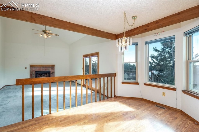 spare room with vaulted ceiling with beams, a textured ceiling, a fireplace, ceiling fan with notable chandelier, and hardwood / wood-style flooring