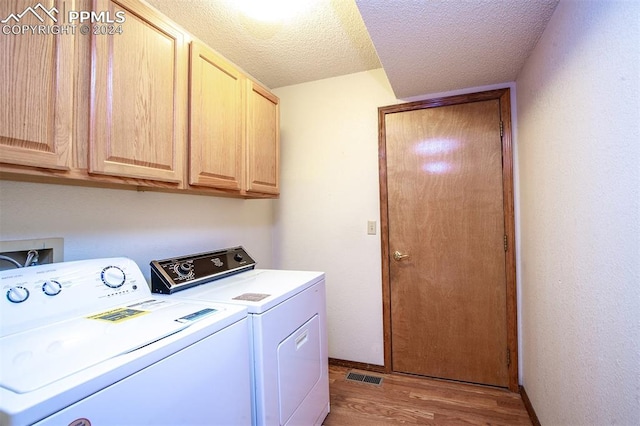 clothes washing area featuring cabinets, light hardwood / wood-style flooring, washer and dryer, and a textured ceiling