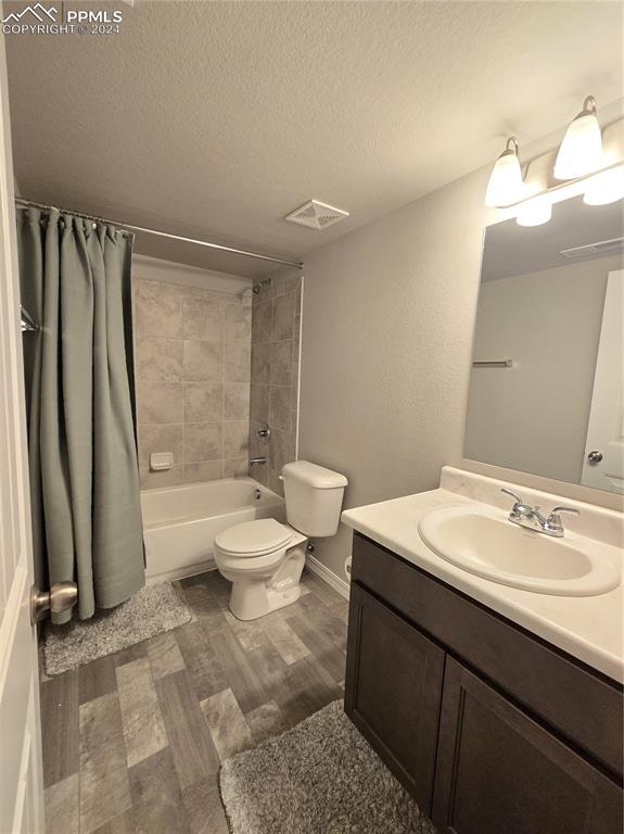 full bathroom with hardwood / wood-style floors, vanity, toilet, shower / bath combo with shower curtain, and a textured ceiling