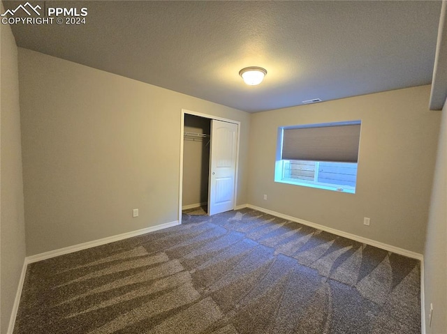 unfurnished bedroom with a textured ceiling, dark carpet, and a closet