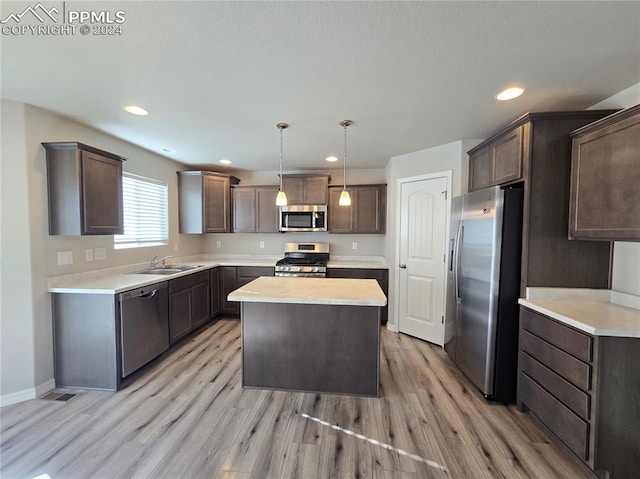 kitchen featuring decorative light fixtures, stainless steel appliances, a kitchen island, and light hardwood / wood-style floors