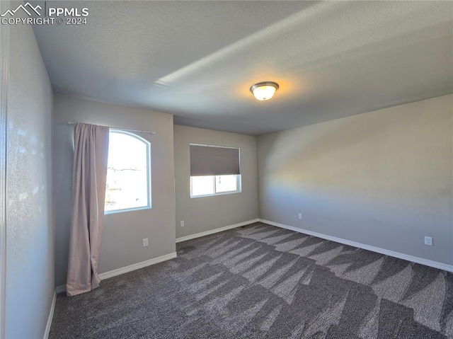 unfurnished room featuring dark carpet and a textured ceiling