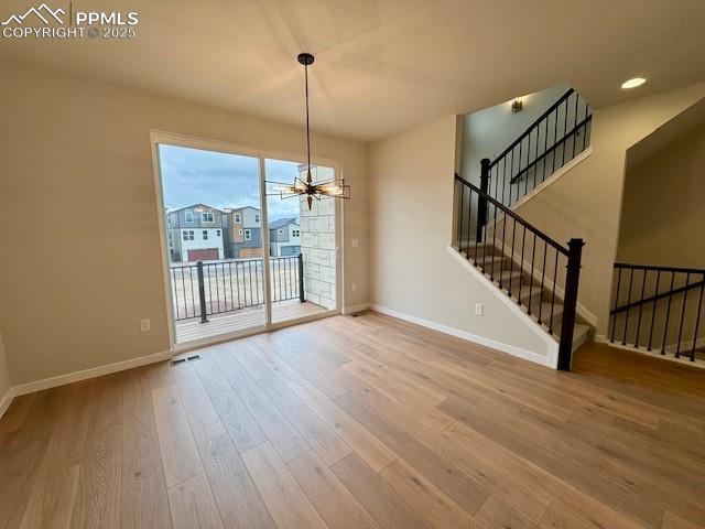 unfurnished dining area featuring stairs, baseboards, an inviting chandelier, and wood finished floors