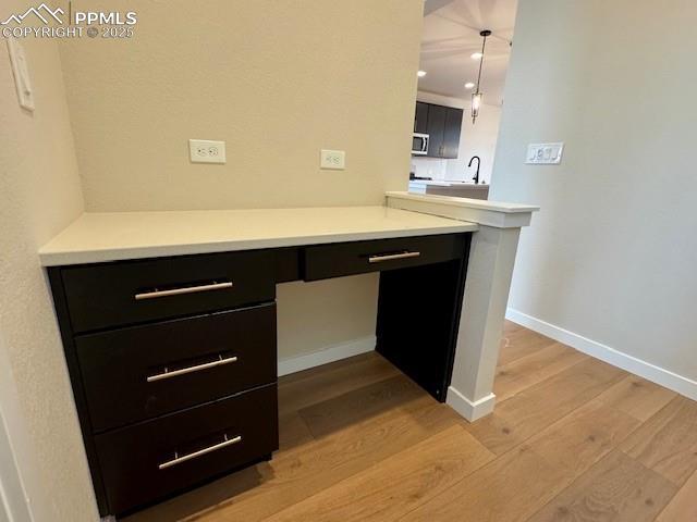 bar with stainless steel microwave, built in desk, baseboards, light wood finished floors, and a sink
