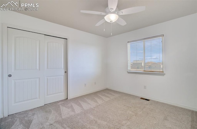 unfurnished bedroom featuring a closet, light colored carpet, and ceiling fan