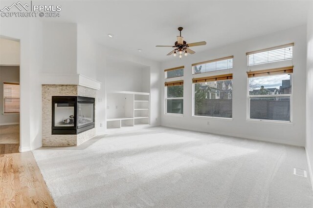 unfurnished living room featuring a multi sided fireplace, light carpet, built in features, and ceiling fan