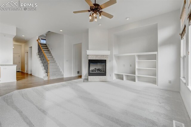 unfurnished living room with built in shelves, ceiling fan, a multi sided fireplace, and light carpet