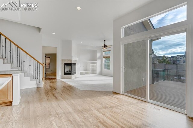 unfurnished living room with a multi sided fireplace, ceiling fan, a healthy amount of sunlight, and light hardwood / wood-style floors