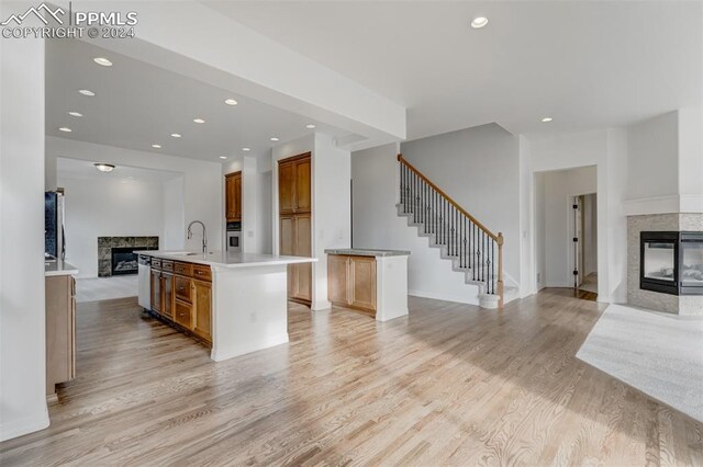 kitchen with sink, a multi sided fireplace, an island with sink, oven, and light wood-type flooring