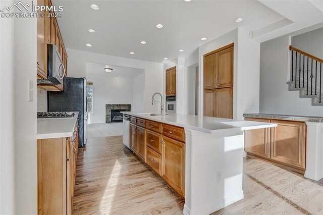 kitchen with appliances with stainless steel finishes, backsplash, a kitchen island with sink, sink, and a tile fireplace