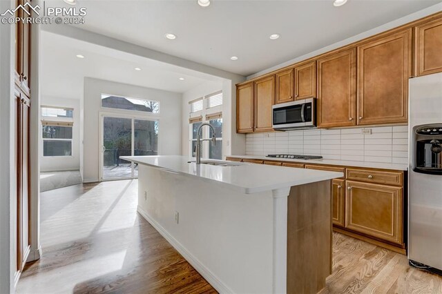 kitchen featuring backsplash, a center island with sink, sink, appliances with stainless steel finishes, and light hardwood / wood-style floors