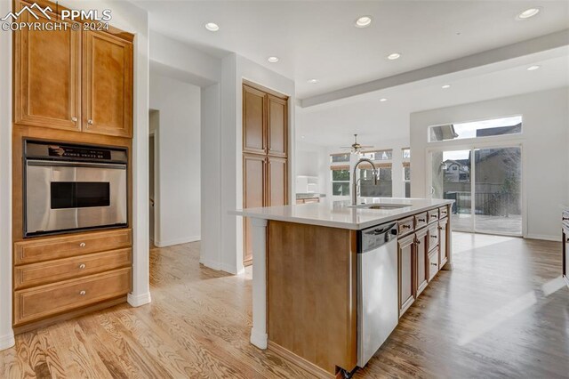 kitchen with ceiling fan, sink, stainless steel appliances, light hardwood / wood-style flooring, and an island with sink