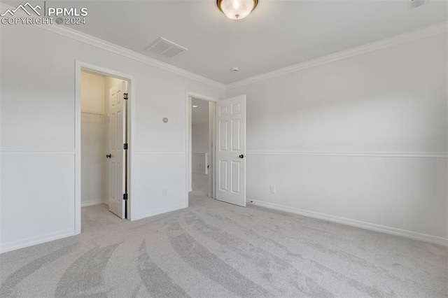 unfurnished bedroom featuring light carpet, a walk in closet, a closet, and ornamental molding