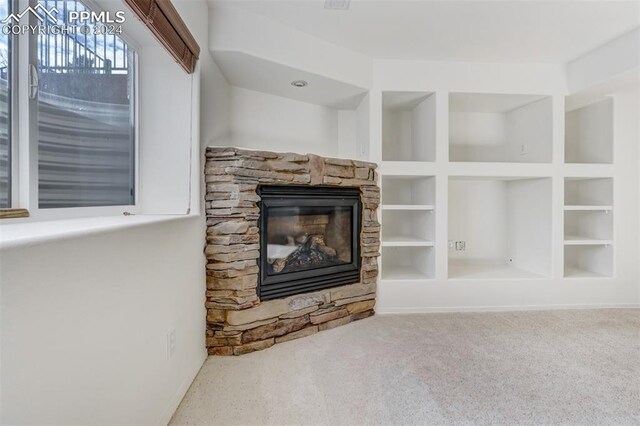 unfurnished living room with carpet floors, built in features, and a stone fireplace