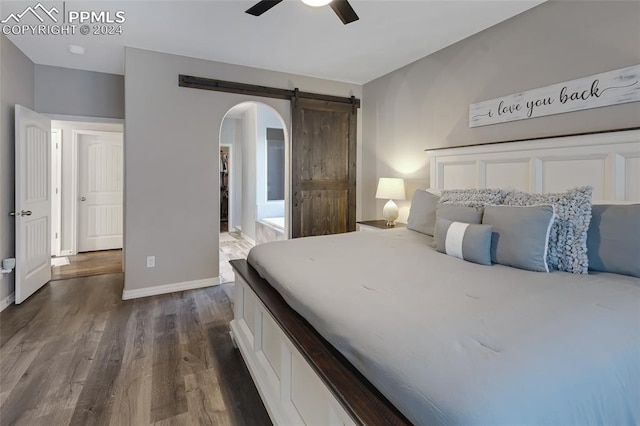 bedroom with a barn door, dark hardwood / wood-style floors, and ceiling fan