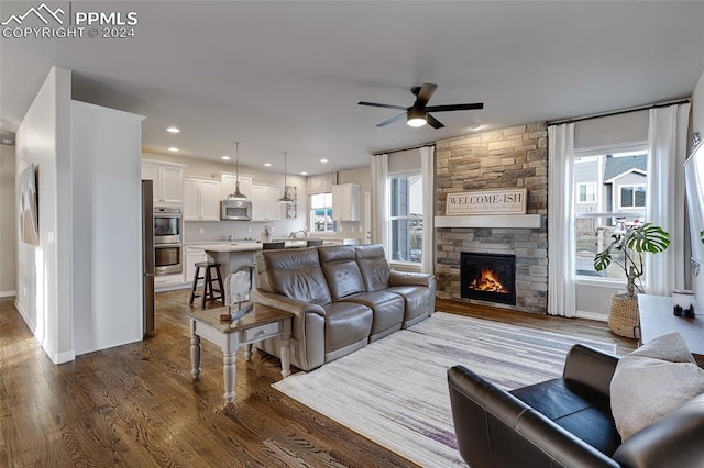 living room with dark hardwood / wood-style floors, ceiling fan, and a stone fireplace