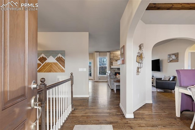 foyer entrance featuring beam ceiling, a stone fireplace, and dark wood-type flooring