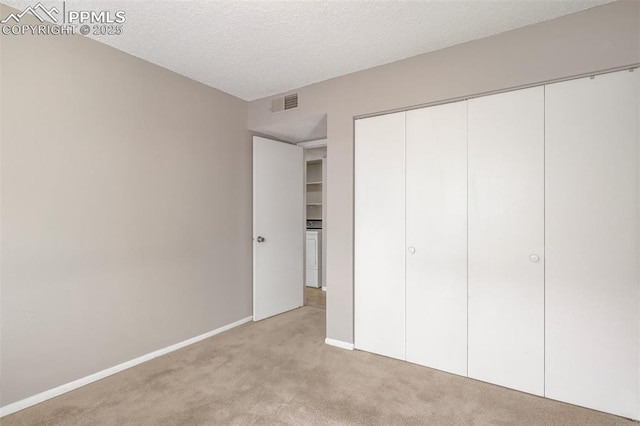 unfurnished bedroom with a textured ceiling, washer / clothes dryer, a closet, and light carpet