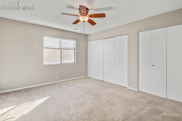 unfurnished bedroom with ceiling fan, light colored carpet, multiple closets, and a textured ceiling