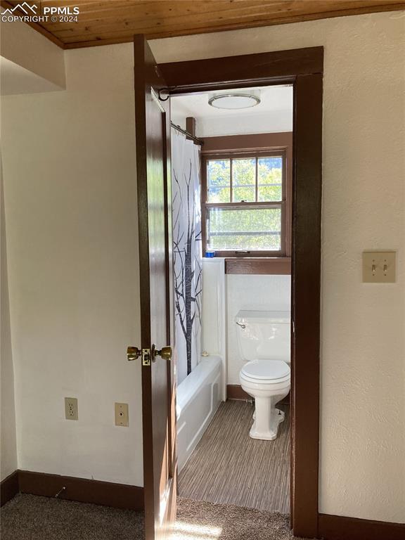 bathroom with toilet, shower / bathtub combination with curtain, and baseboards