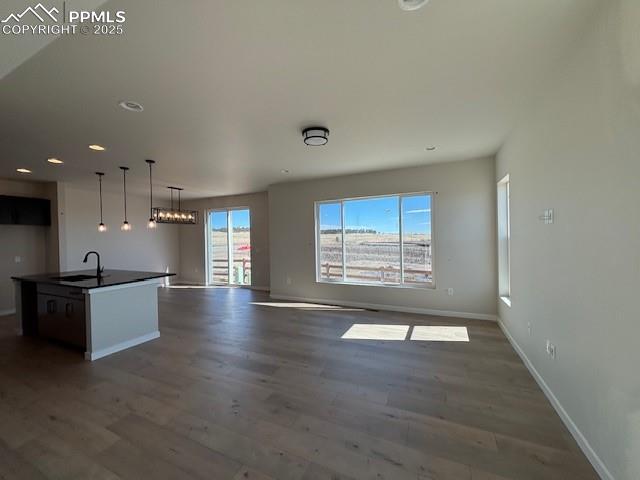 kitchen featuring a center island with sink, dark countertops, dark wood-style floors, open floor plan, and a sink