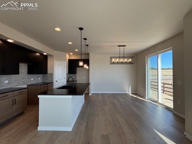 kitchen featuring tasteful backsplash, dark countertops, modern cabinets, a kitchen island with sink, and a sink