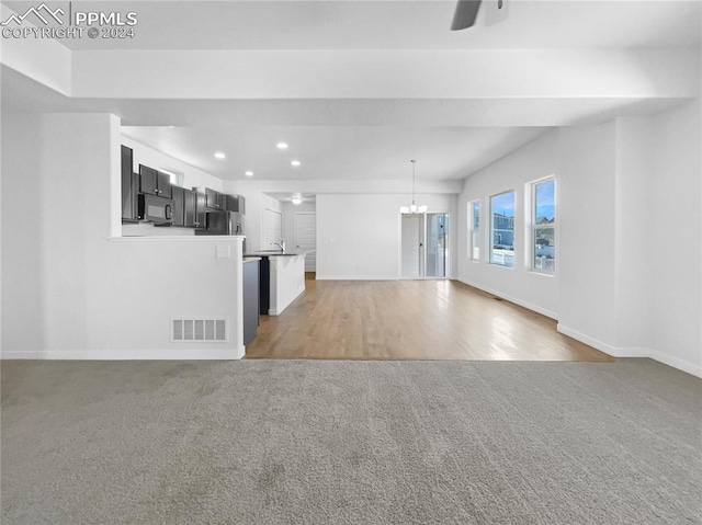 unfurnished living room featuring hardwood / wood-style floors, ceiling fan with notable chandelier, and sink