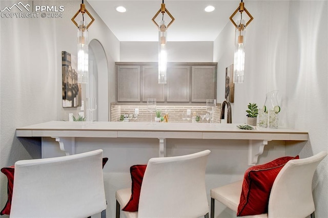 interior space with decorative backsplash, gray cabinets, sink, and hanging light fixtures